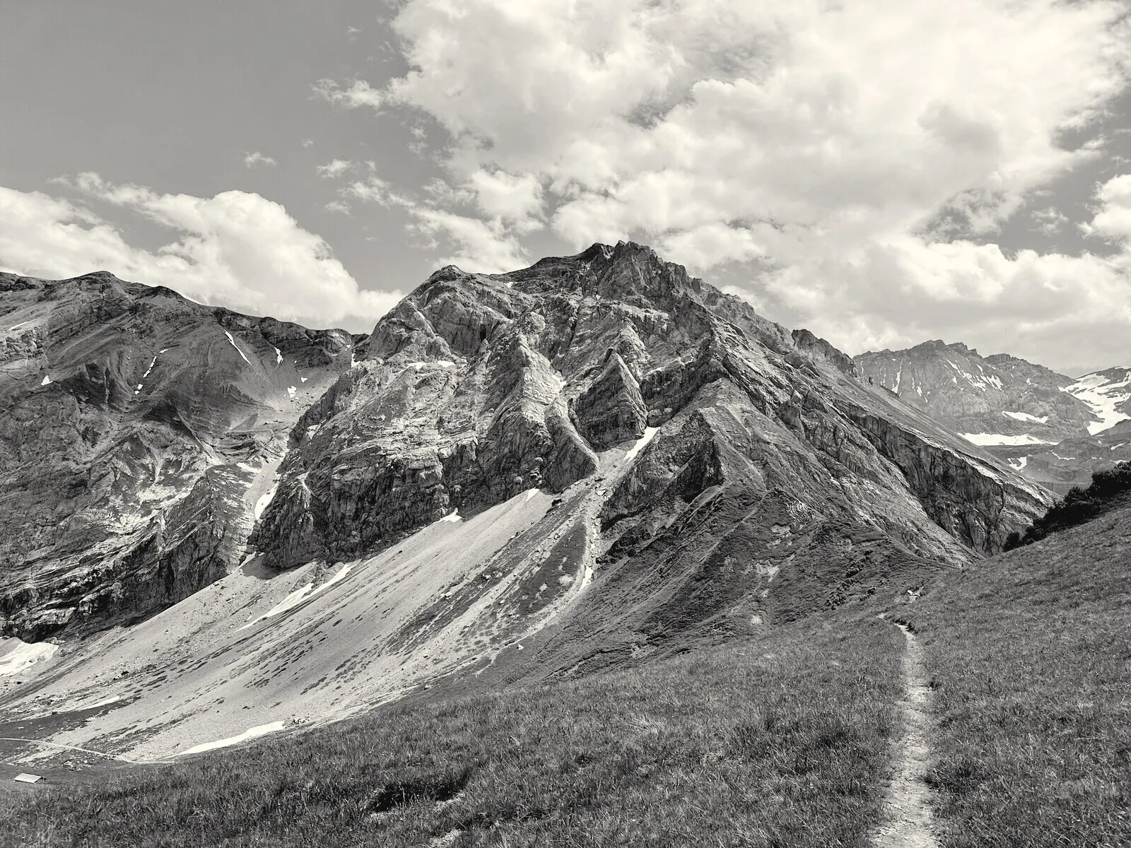 A mountain ridge above Lenk in black and white, a path running up to it.