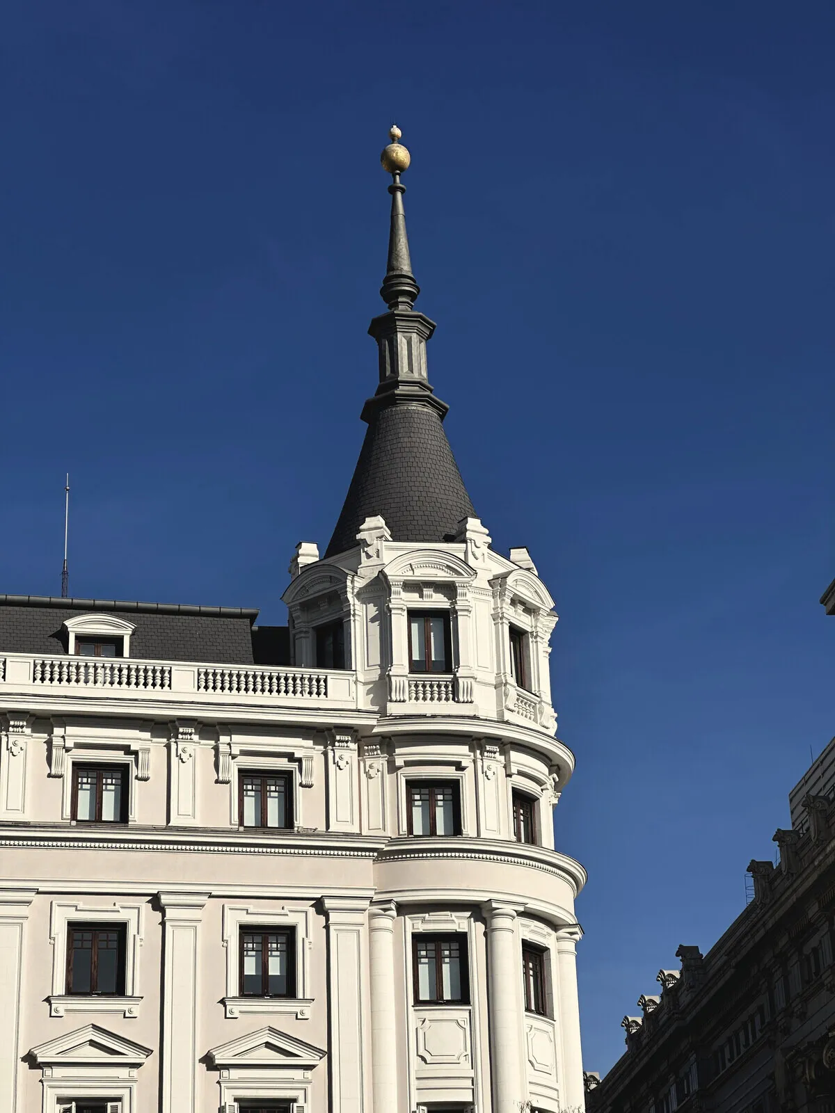 A white building in Madrid with a dark spire, against blue sky.