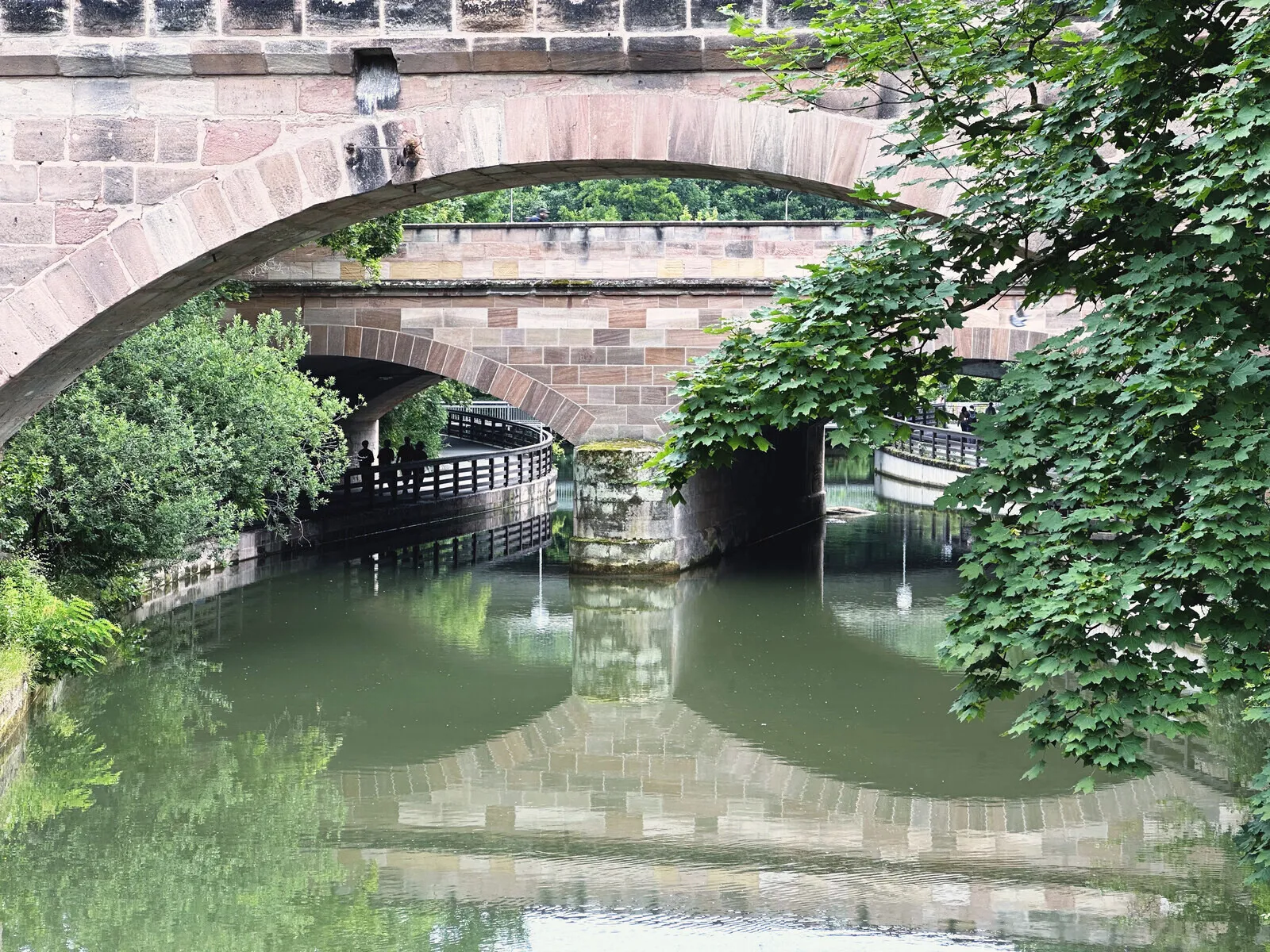 A stone bridge in Nuremberg reflected in the water under it.