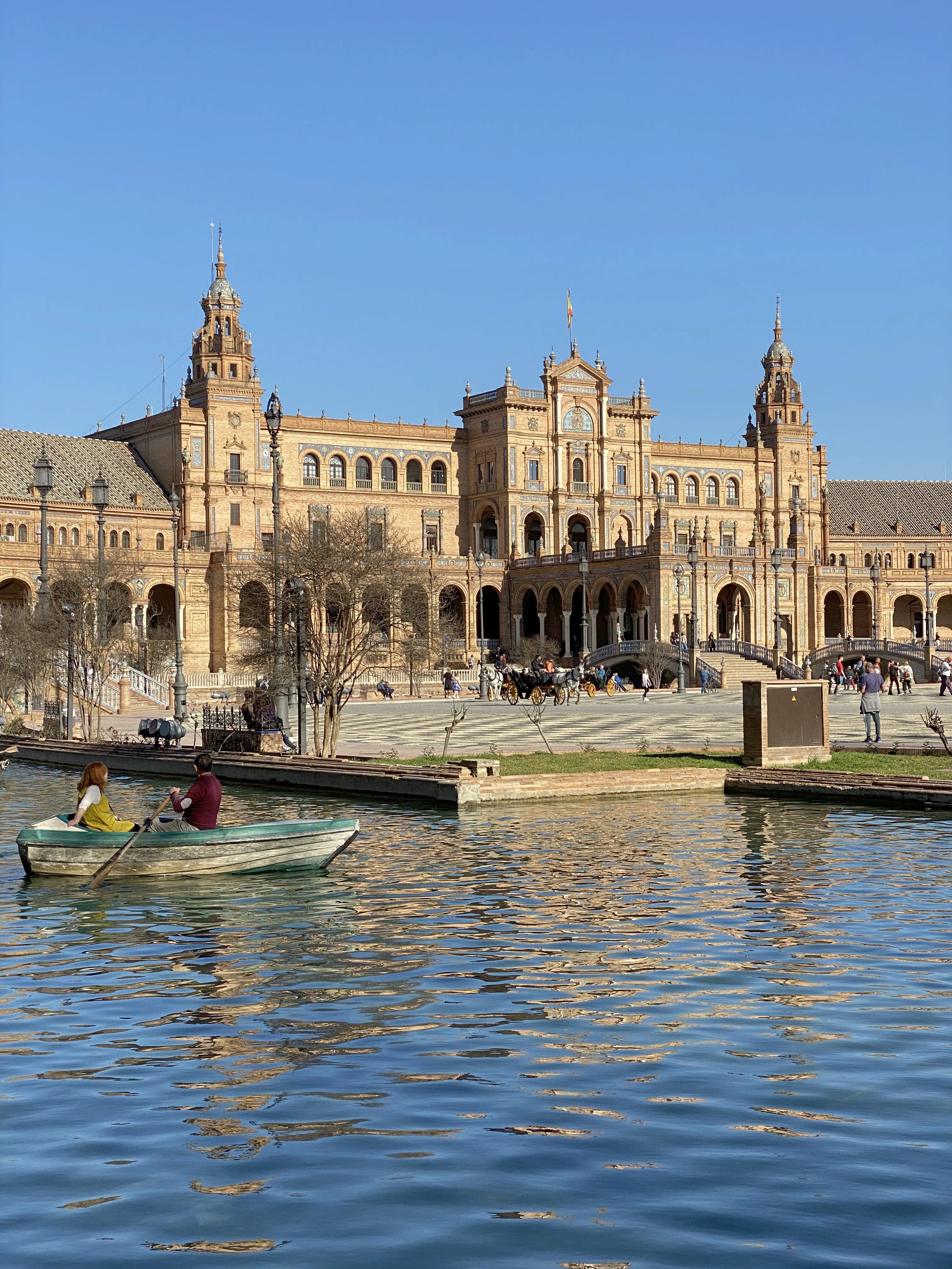 The curved facade of the Plaza de España across the water, a rowing boat in front of it.