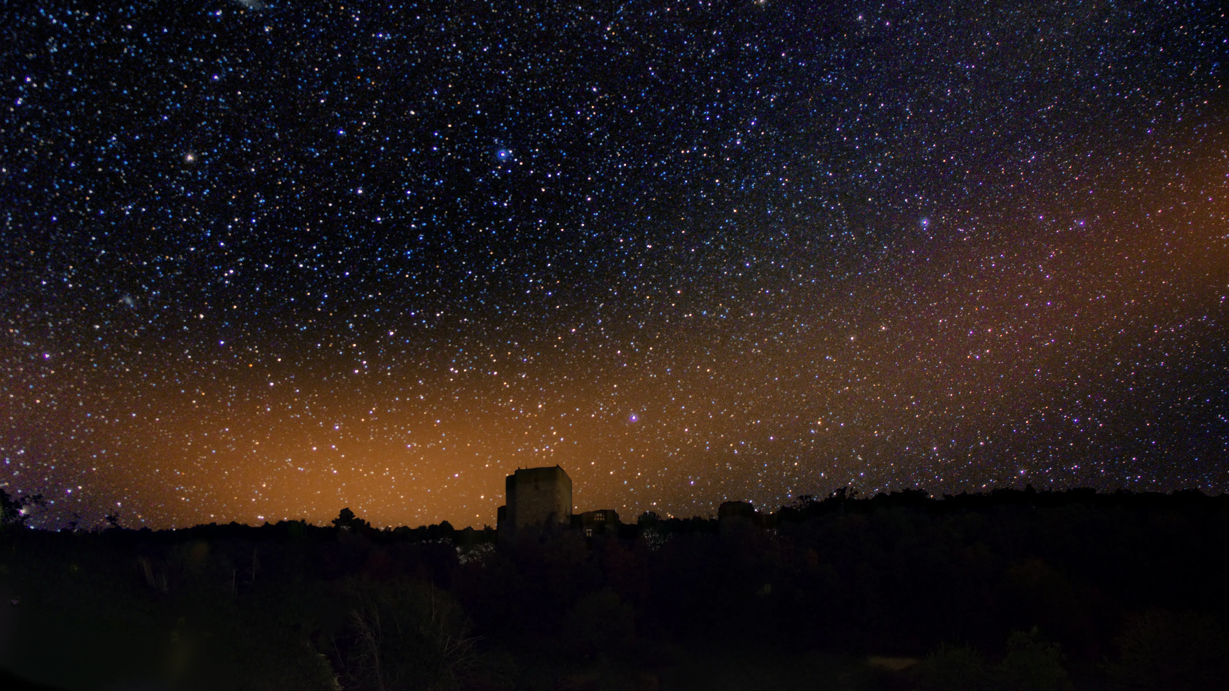 The night sky thick with stars over the dark silhouette of Landskron castle.